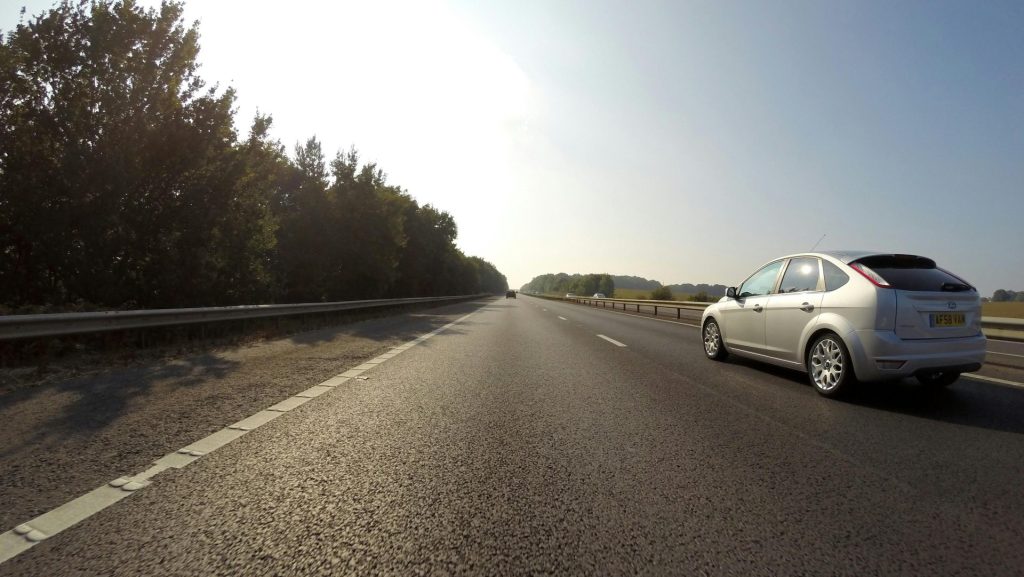 White car traveling on a clear highway in Hatfield, England with scenic trees.